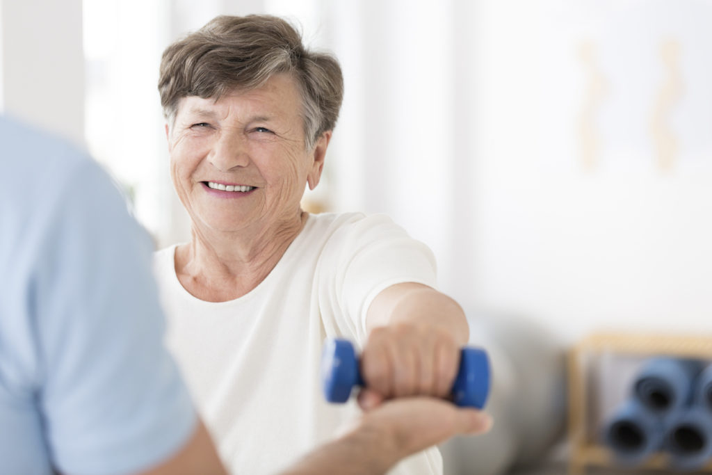 A smiling resident lifting a small dumbbell with assistance from a physical therapist.